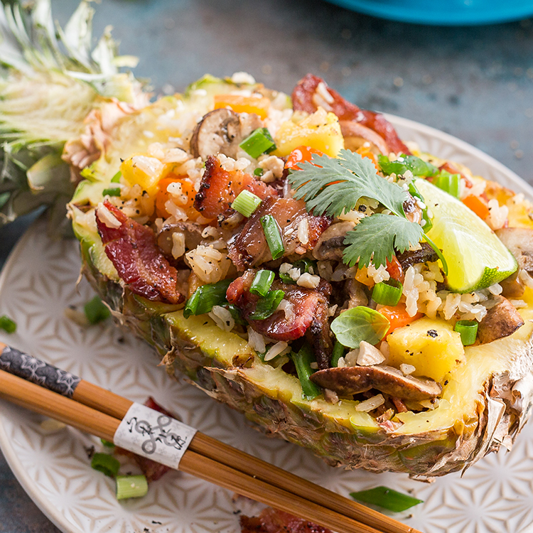 Pineapple fried rice served in half of a pineapple, on a decorative plate.