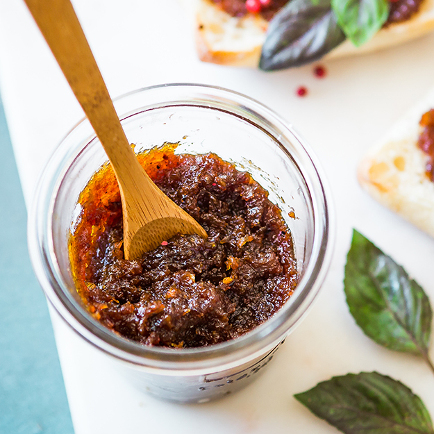 Bacon jam in a jar with a wooden spoon, bright background with basil leaves.