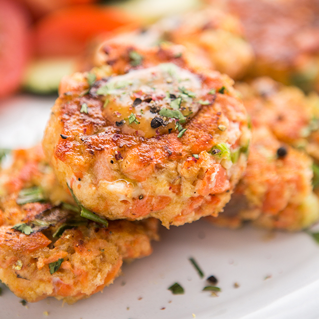 Salmon patties garnished with sriracha sauce and herbs on a plate, close-up view.