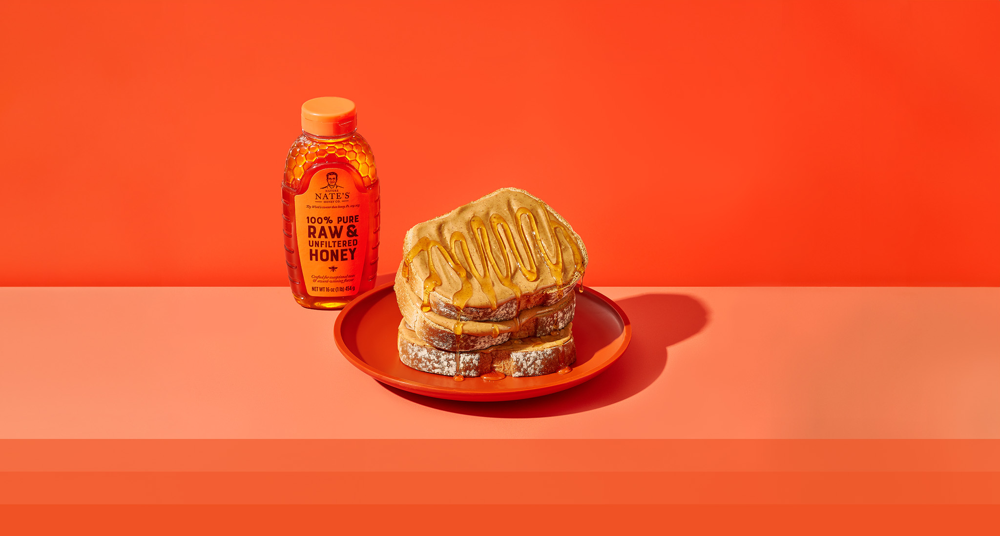 Three slices of peanut butter toast stacked with honey drizzled all over toast stack. Next to Nate's honey bottle.