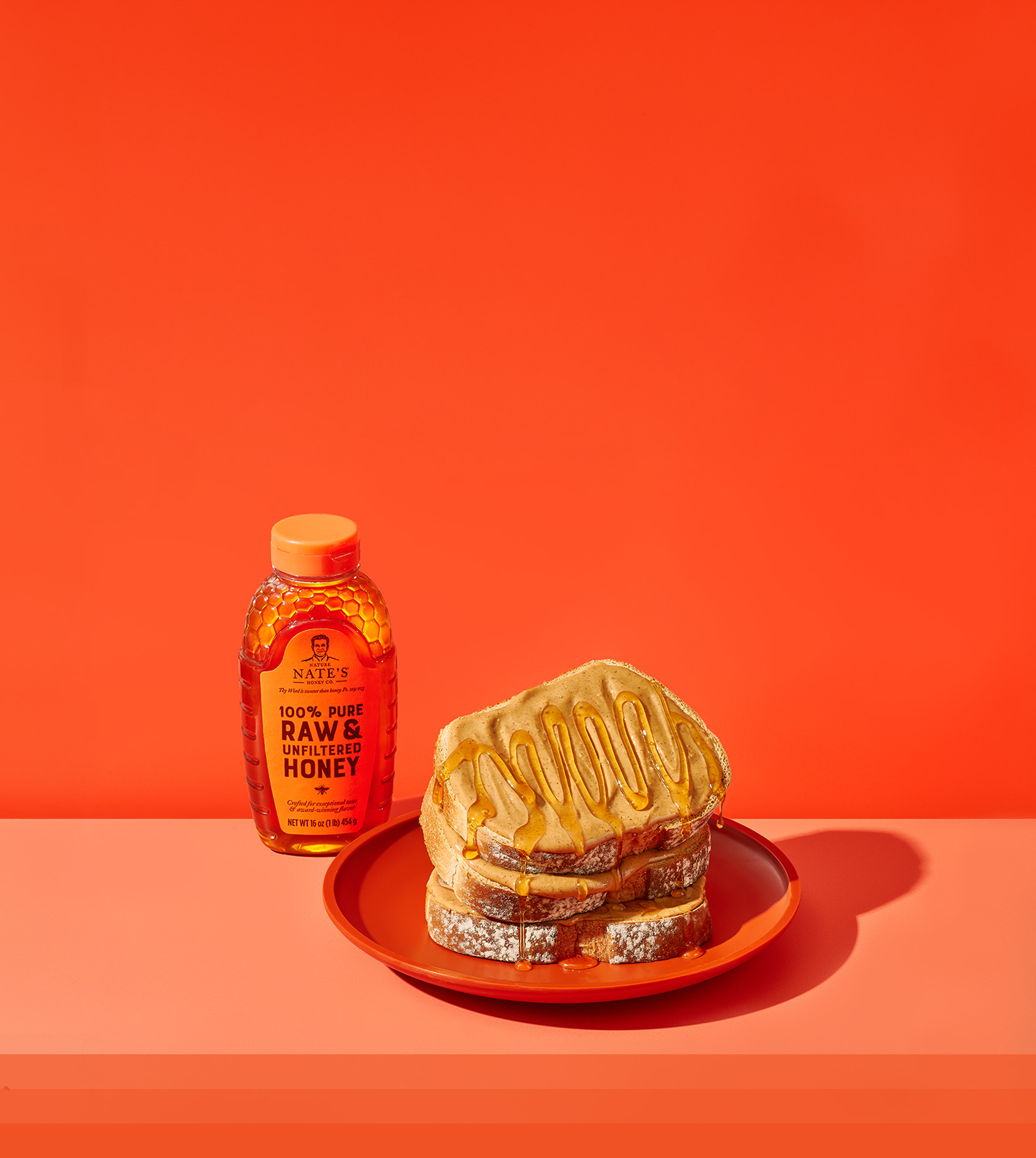 Bottle of Nate's Honey next to plate of toast with peanut butter and honey on orange background