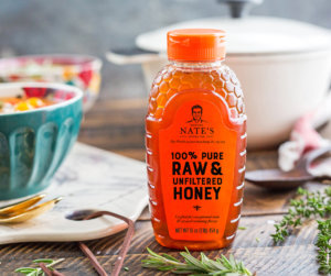 Nate's honey bottle on table with salad bowl and wooden spoon, fresh thyme sprigs nearby.