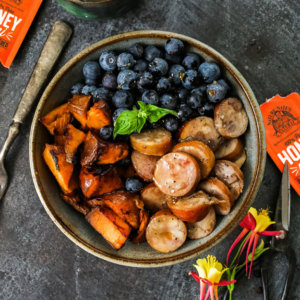 Healthy meal in a bowl with blueberries, vegetables and sausage with Nate's honey minis on a dark textured background.