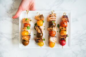 A hand presenting a platter of colorful mixed grill skewers on a marble surface, perfect for gatherings.