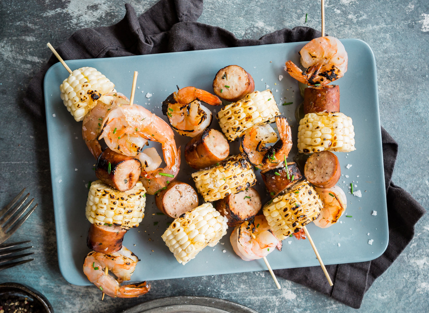 Grilled shrimp and sausage skewers with corn pieces on a plate, a fusion of flavors for BBQ or outdoor cooking.