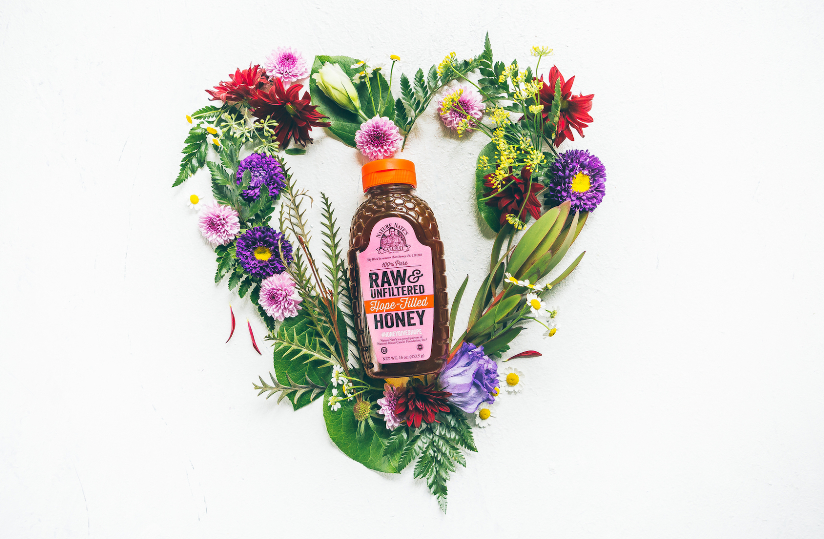 A bottle of Nate's honey centered in a heart-shaped arrangement of colorful wildflowers against a white background.