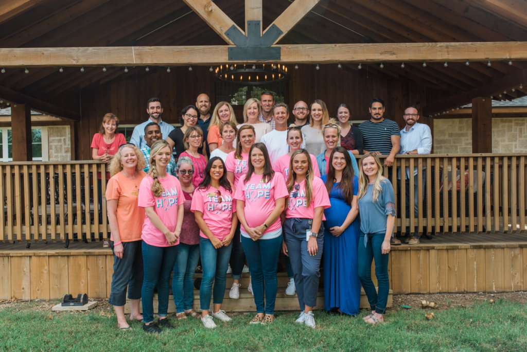 A group of people in pink shirts and other colored shirts smiling in front of a building, some shirts say Team Hope.