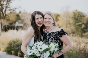 Two joyful women smiling, one holding a bouquet, creating a cherished memory together.