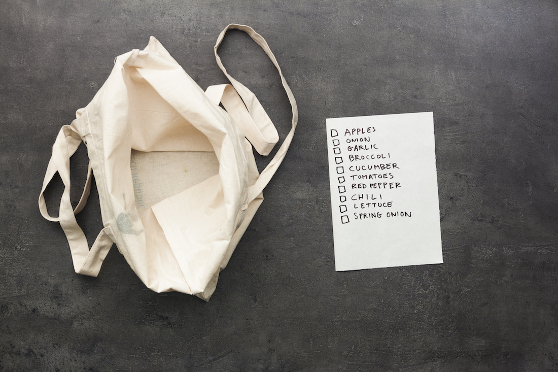 Empty tote bag with a grocery checklist on a gray background.
