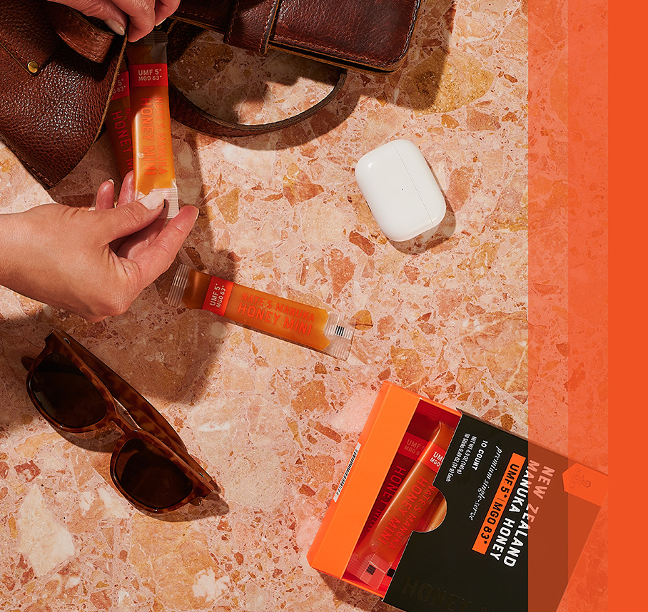 Manuka Honey Mini sticks placed on a marble surface alongside a bag, sunglasses, and AirPods.