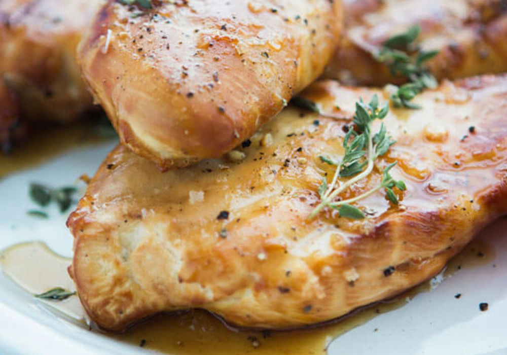 Grilled chicken breasts seasoned with herbs on a plate, showcasing a golden-brown sear and juicy appearance.