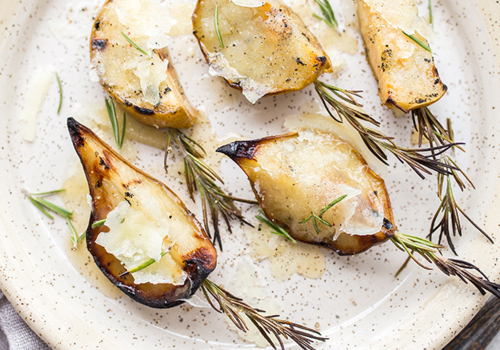 Roasted pears with cheese, rosemary and a drizzle of honey on a speckled plate.