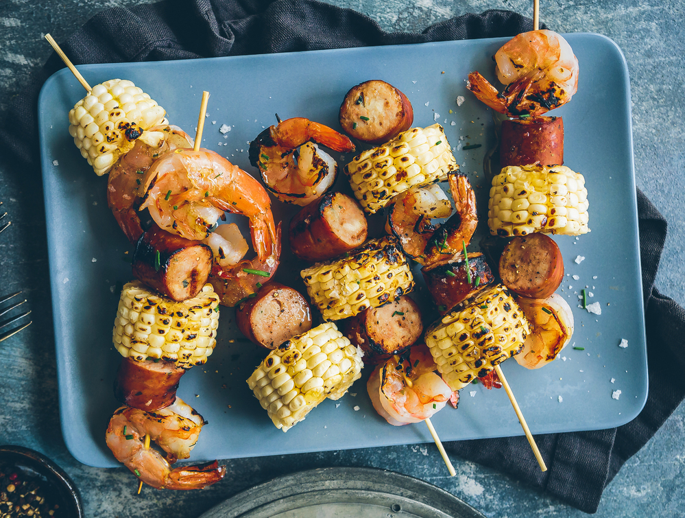 blue table and blue plate with skewers of grilled sausage, shrimp and corn