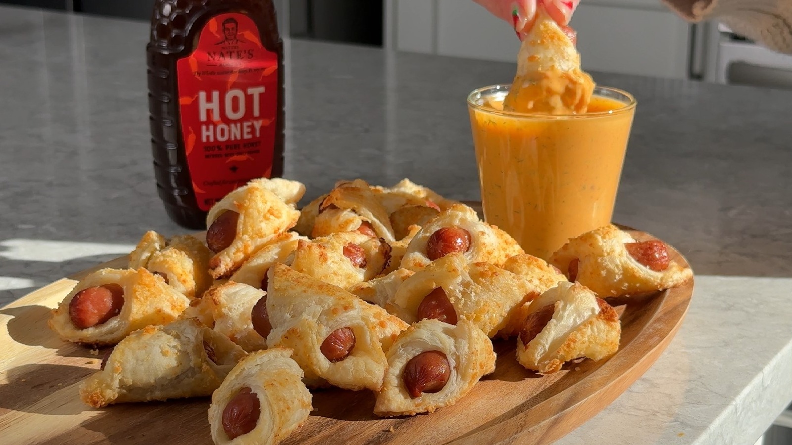 Nate’s Hot Honey with pigs in a blanket on a wooden board, served with a hot honey dipping sauce.