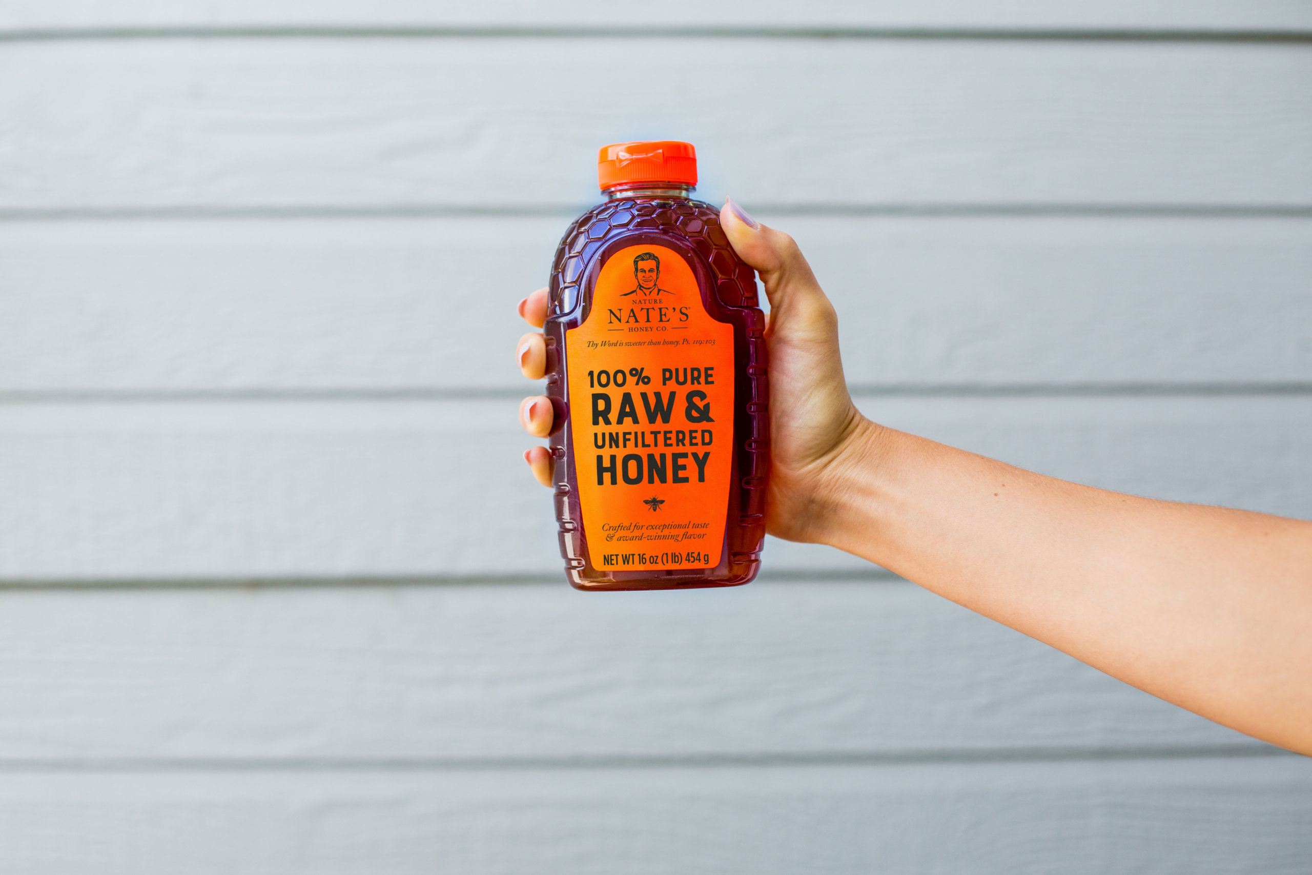Hand holding a bottle of Nate's honey against a gray wooden backdrop.