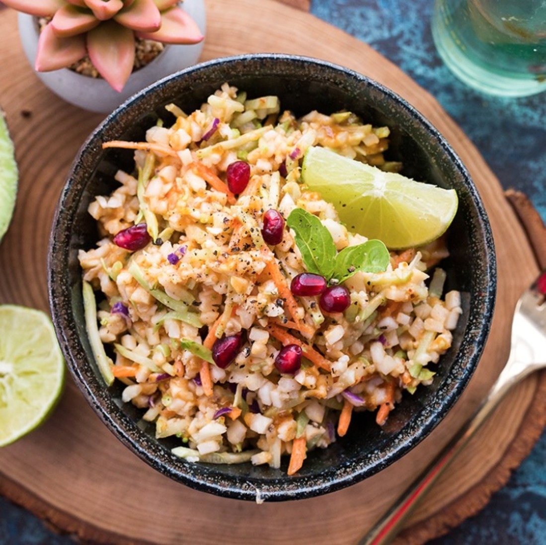 Raw veggie salad in a bowl with lime wedges and pomegranate seeds, on a blue textured surface. Raw veggie salad in a bowl with lime wedges and pomegranate seeds, on a blue textured surface.