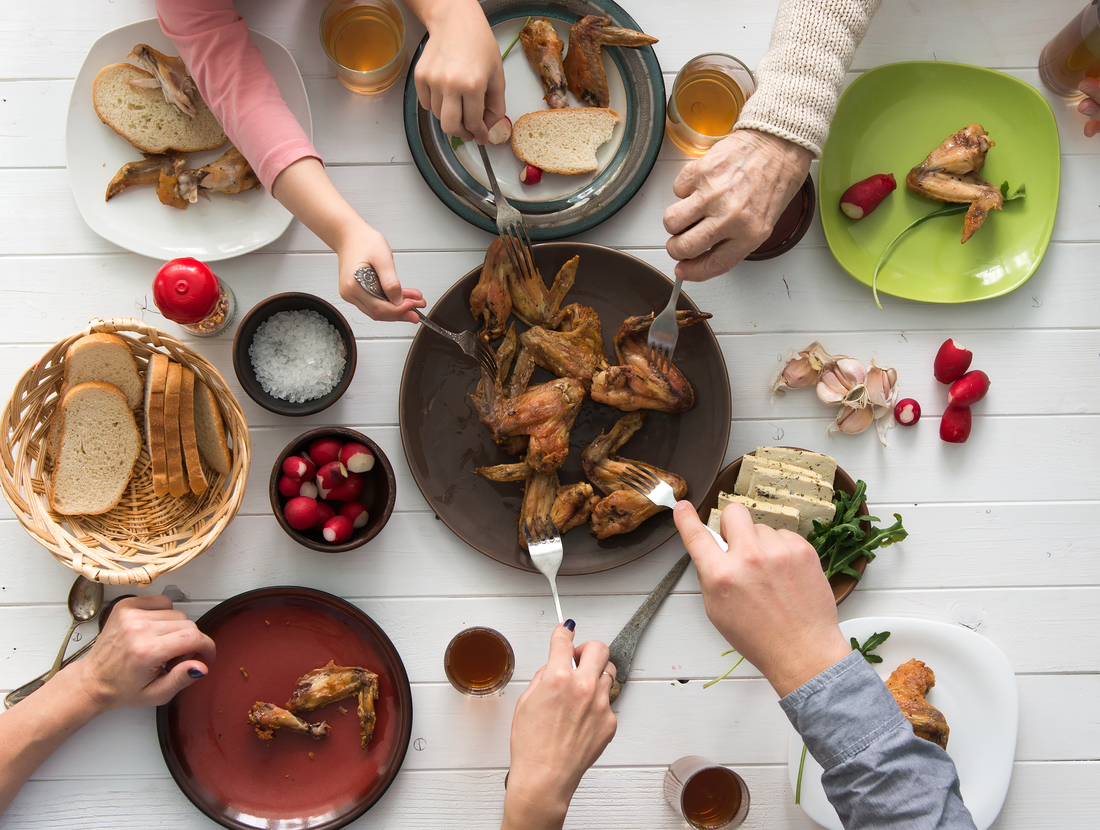 Family dining on chicken wings with sides and bread on the table.