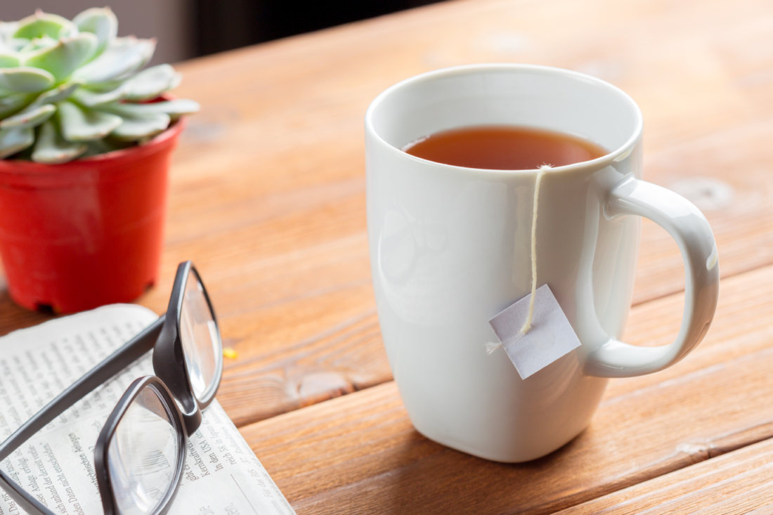 Teacup with teabag, glasses, and plant on a wooden table. Teacup with teabag, glasses, and plant on a wooden table.