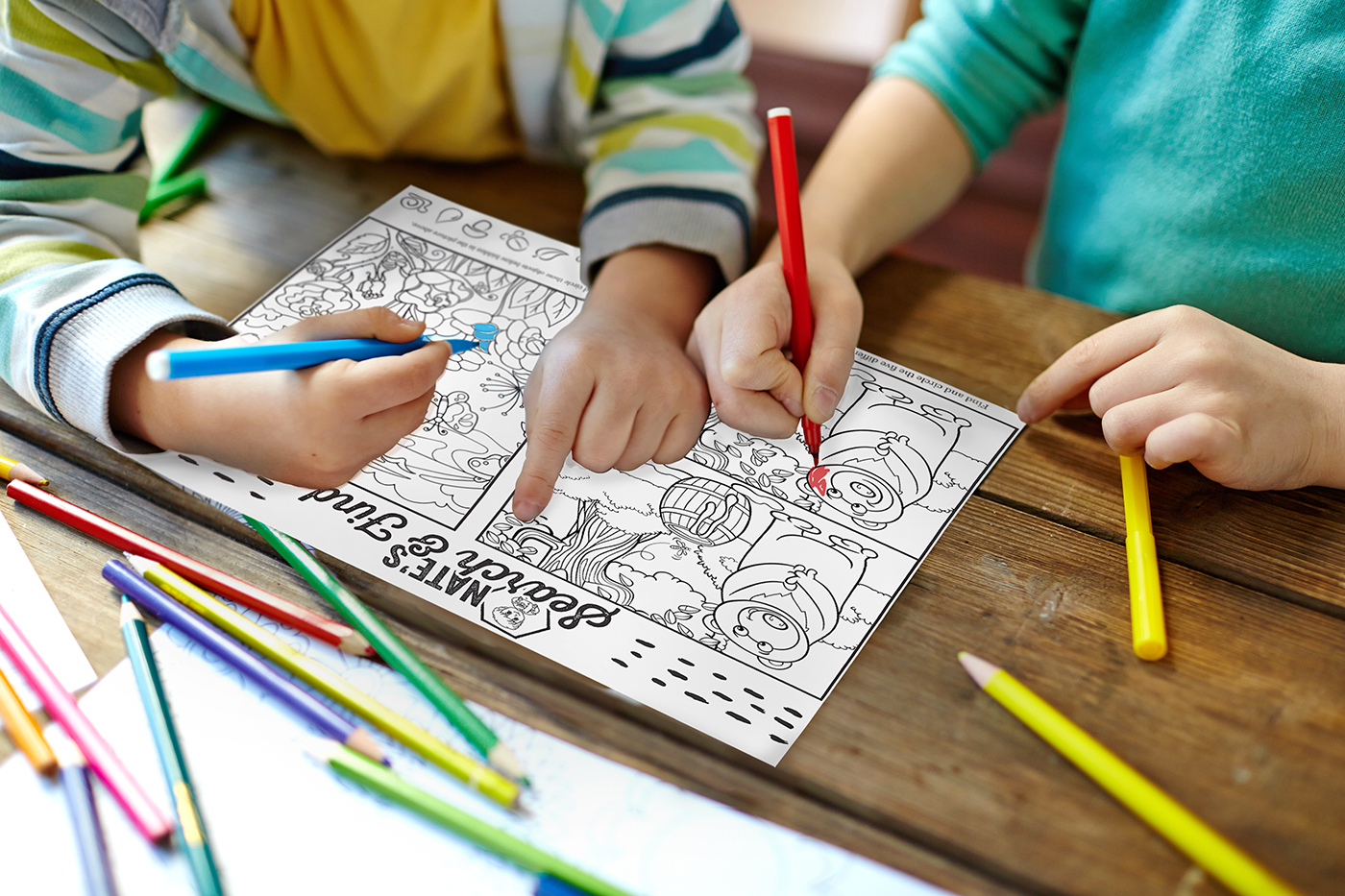 Two children coloring with pencils, coloring book and scattered pencils on a table.