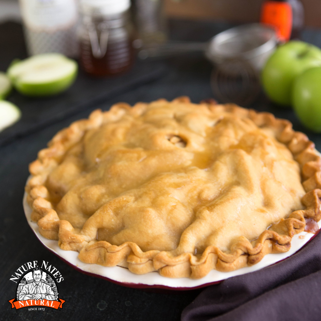 Golden pie on a plate, Nature Nate's logo, green apples background, cozy kitchen setting. Golden pie on a plate, Nature Nate's logo, green apples background, cozy kitchen setting.
