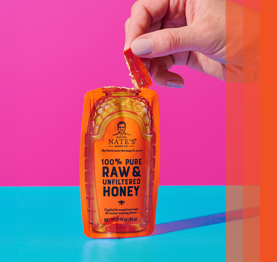 Honey mini resembling small honey bottle standing upright with hand tearing top off that resembles a cap being opened.