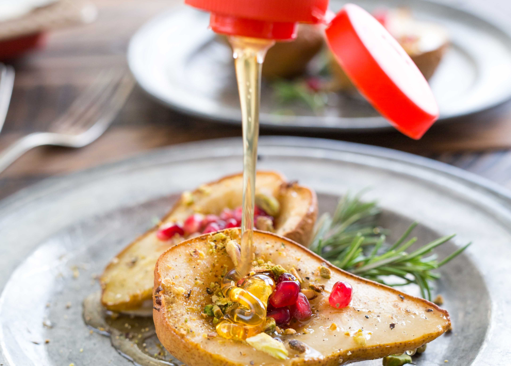 Nate’s honey is being drizzled onto a grilled pear garnished with pomegranate and rosemary on a rustic metal plate. Nate’s honey is being drizzled onto a grilled pear garnished with pomegranate and rosemary on a rustic metal plate.