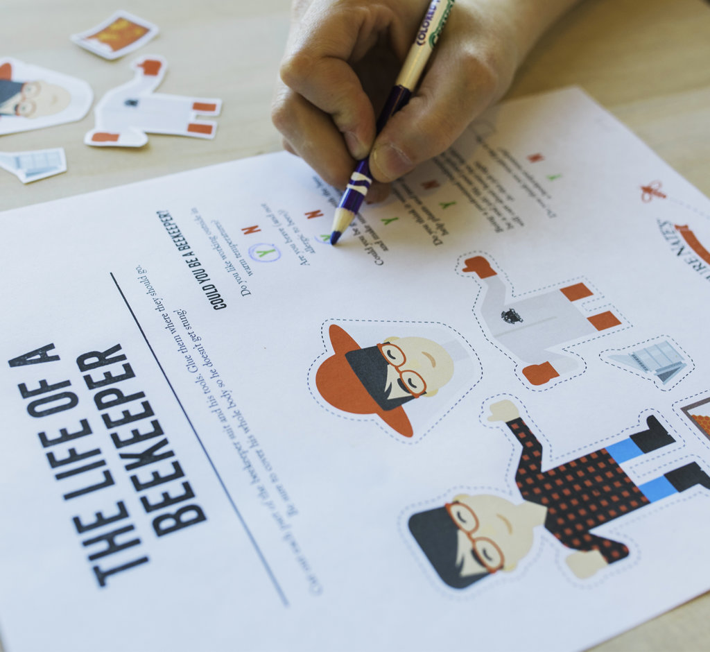 A close-up of a hand filling out a beekeeper's educational activity sheet with illustrations and text. A close-up of a hand filling out a beekeeper's educational activity sheet with illustrations and text.