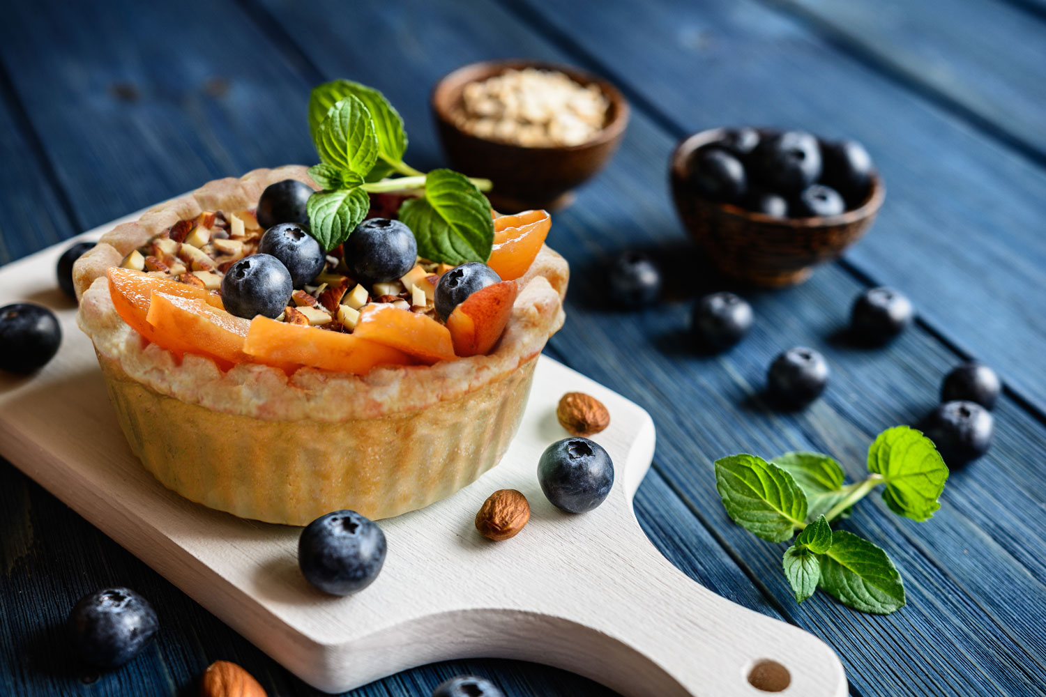 Fresh fruit buckle with blueberries and nuts on a wooden board, dark blue table.