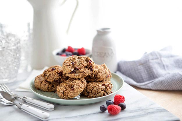 Honey breakfast cookies on a pale blue plate with berries, milk bottle, and a grey napkin on a light table.