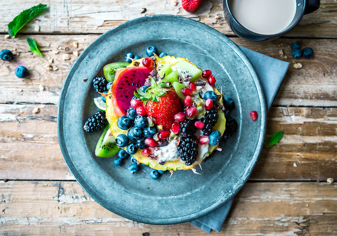 Colorful fruit salad with berries, kiwi, and pomegranate seeds on a blue plate, with a glass of milk on the side.