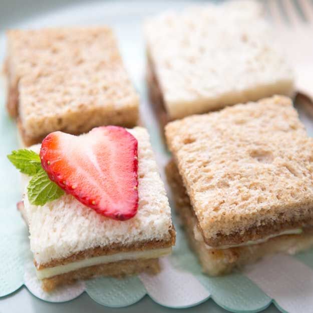 Sandwich squares made with apples, almond butter and honey, and topped with strawberry slices, and mint on a blue doily.