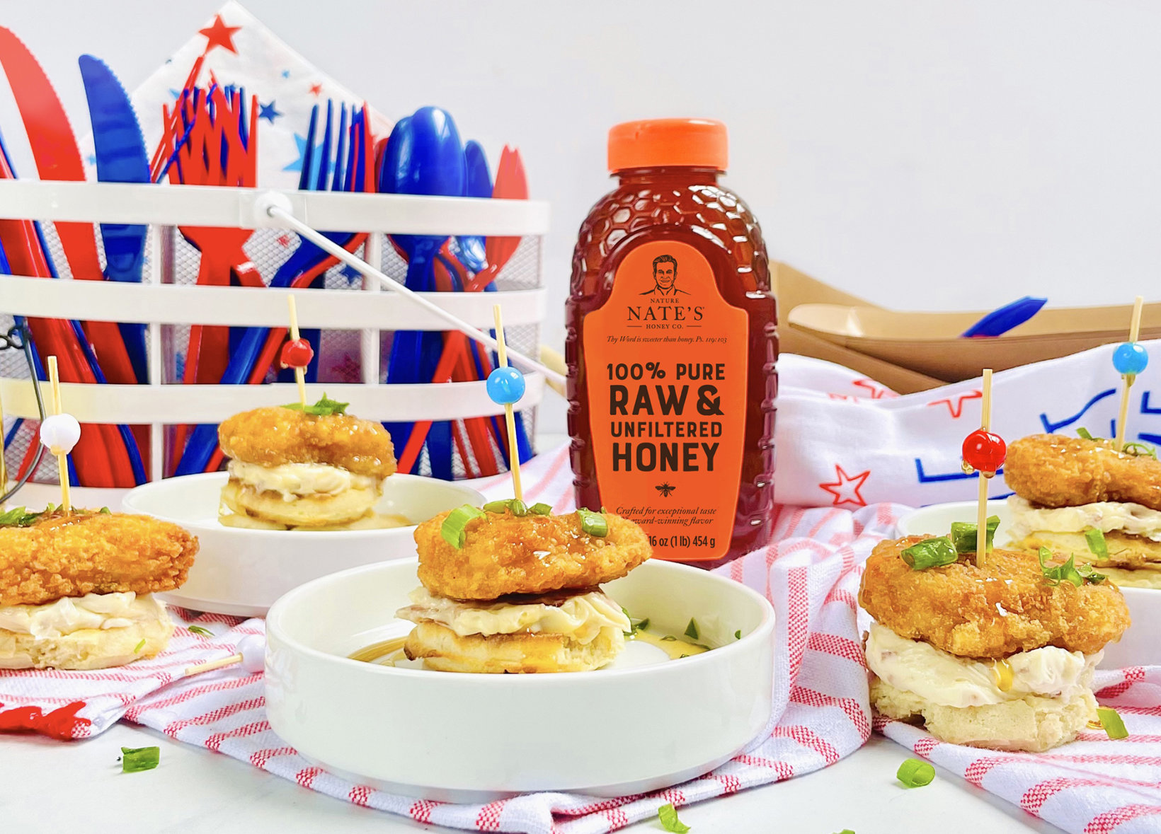 Fried chicken sliders on waffles with a bottle of Nate’s honey, against a festive, patriotic backdrop.