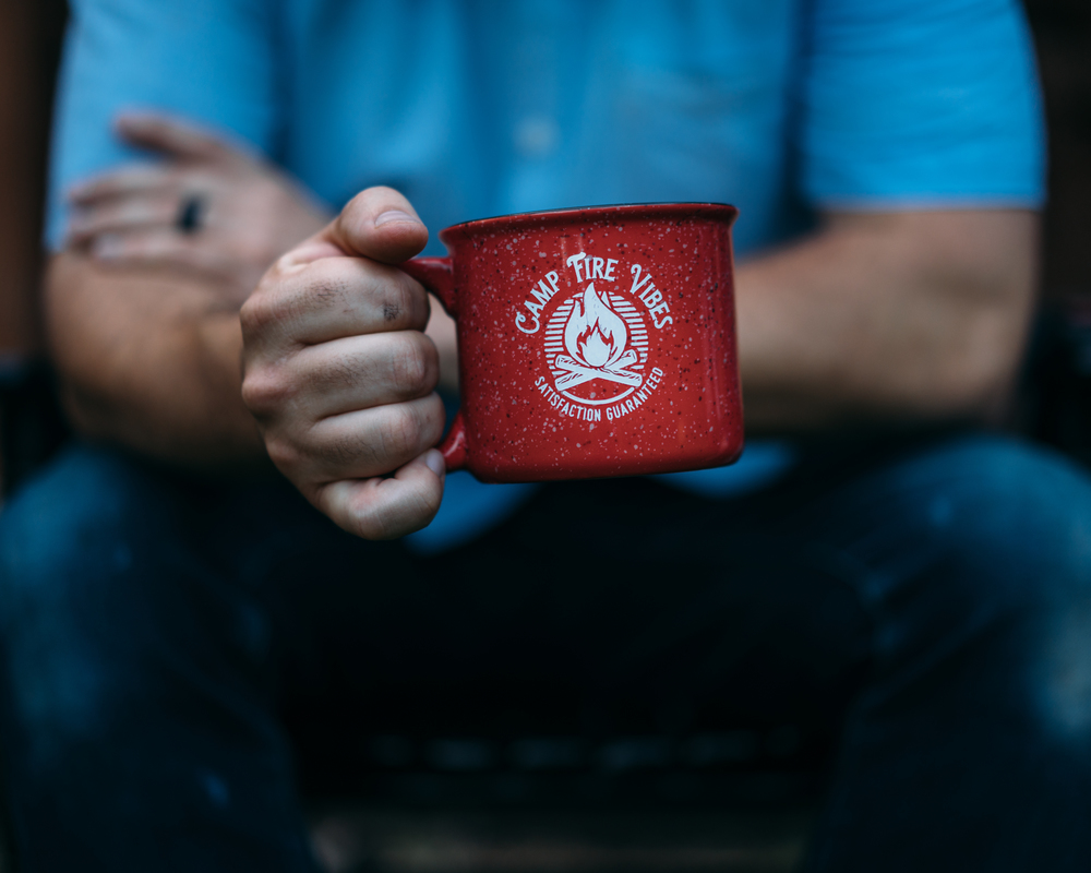 Person holding a red campfire mug with a blurred background.