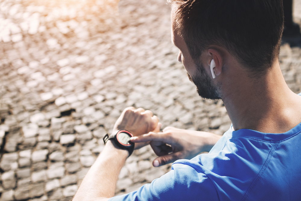 Man checking smartwatch with earphones on a cobbled street.