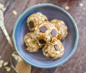 Oatmeal cookie dough bites with chocolate chips in a blue bowl, hinting at a healthy treat, with rustic wood backdrop.