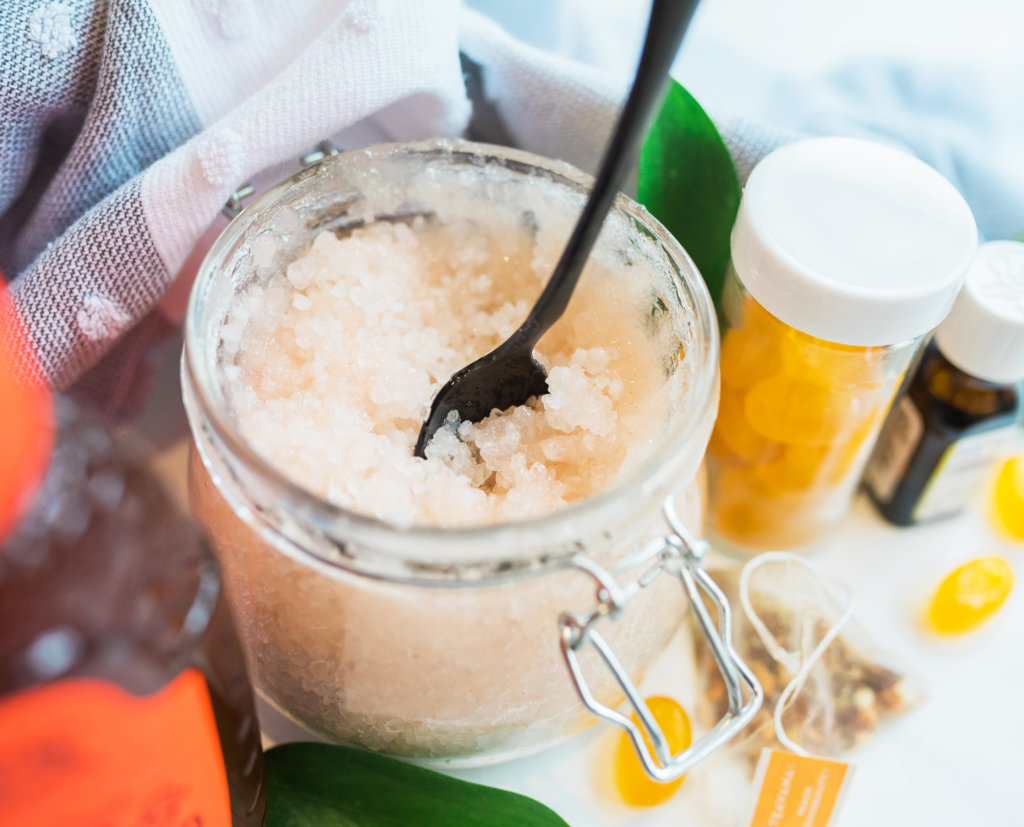 A jar of honey facial scrub with a spoon, essential oils and wellness supplements nearby. A jar of honey facial scrub with a spoon, essential oils and wellness supplements nearby.