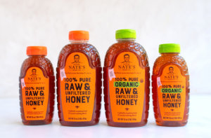 Four bottles of Nature Nate's honey lined up against a white background, featuring varieties of pure, raw, and organic options.