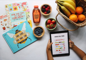 Educational materials with fruits, a Nate's honey bottle, and a child interacting with a tablet.