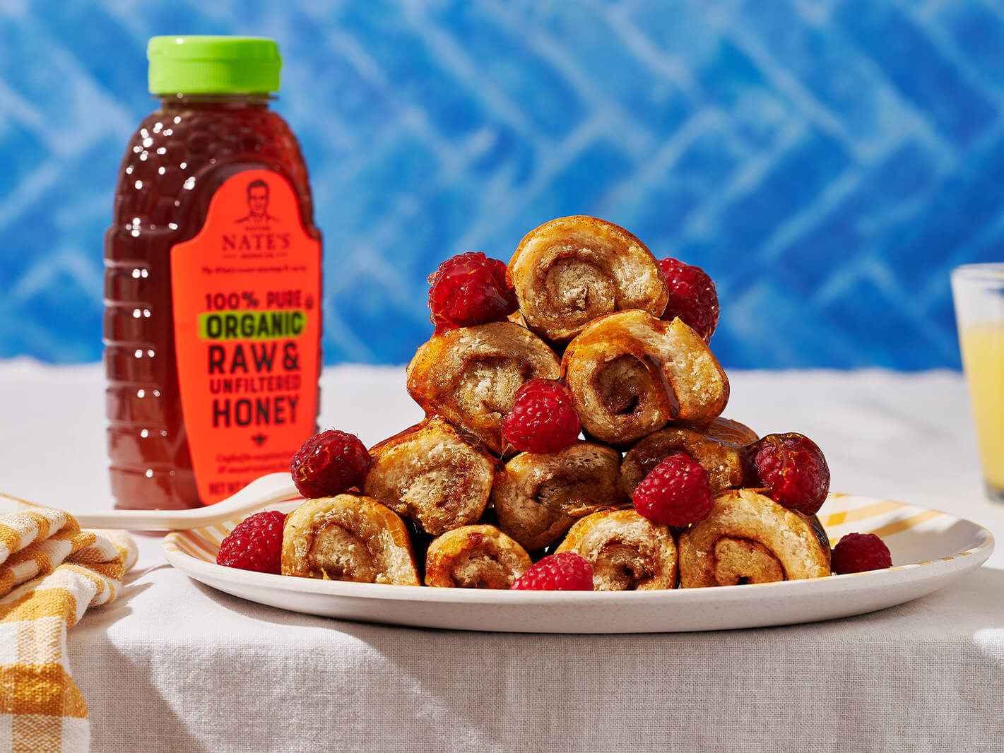 French toast roll-ups with raspberries and a bottle of Nate's organic honey on a white tablecloth.