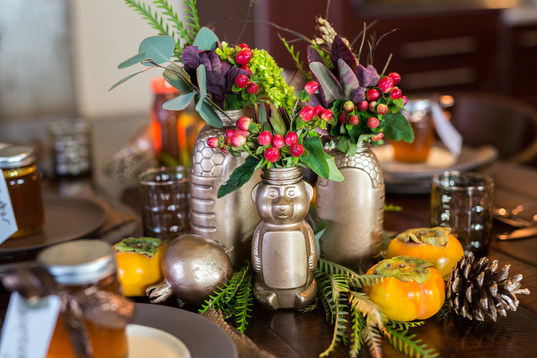 Festive table setting with metallic vases made from Nate's honey bottles and greenery, capturing an autumnal ambiance.