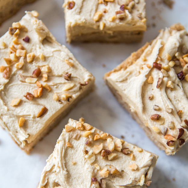 Frosted peanut butter bars topped with chopped nuts on a marble background.