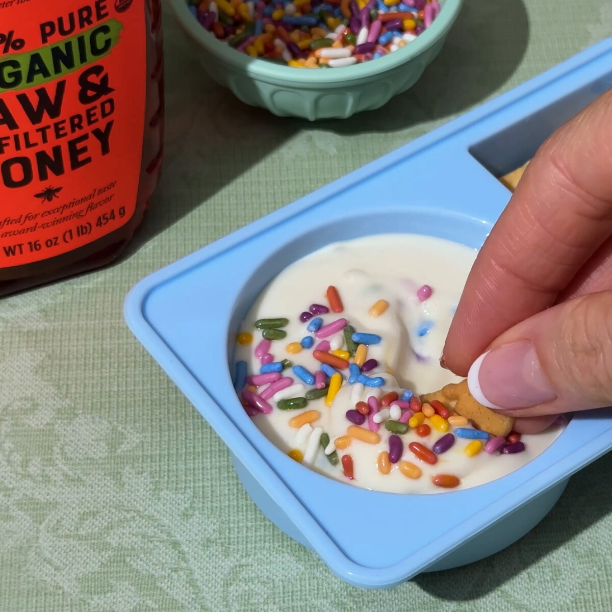 Hand dipping graham cracker into Funfetti Cake Batter Yogurt Dip.