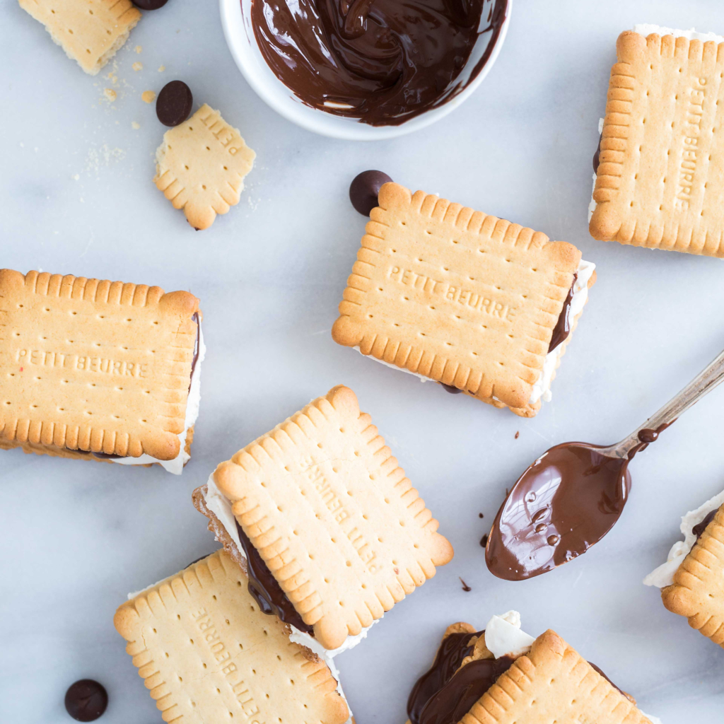 S'mores with chocolate and marshmallow filling, beside melted chocolate, on a marble surface.