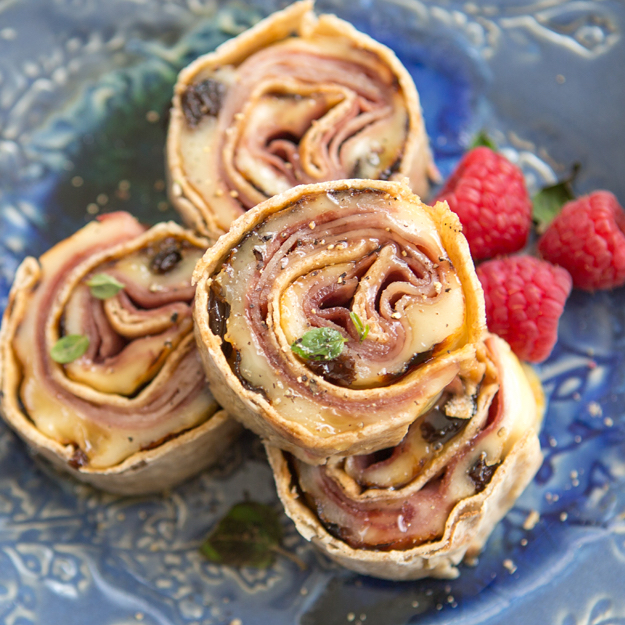 Ham and Swiss cheese rolled in a tortilla, with raspberries on a blue patterned plate.