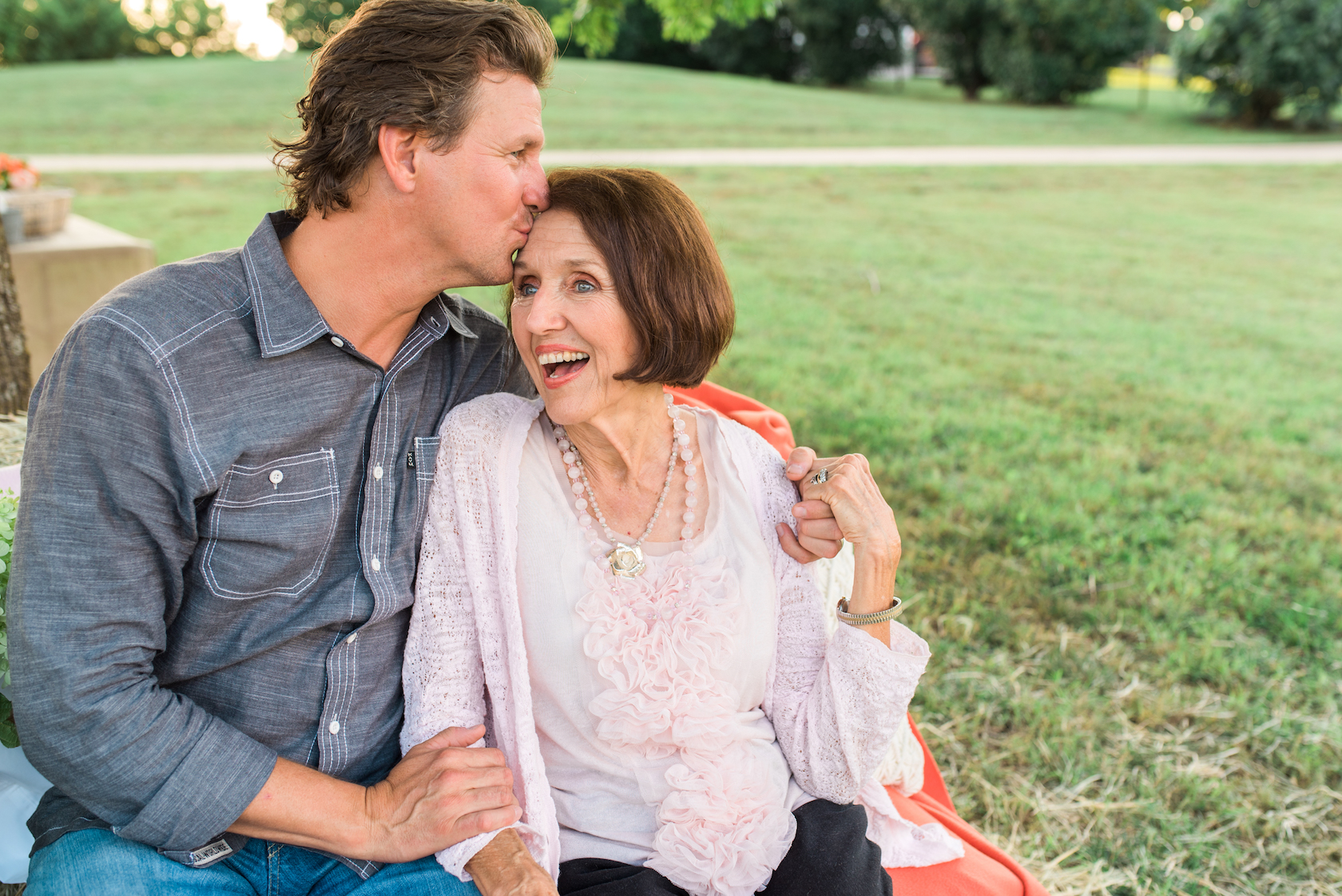 An elderly woman laughing joyfully as nature nates man kisses her cheek outdoors.