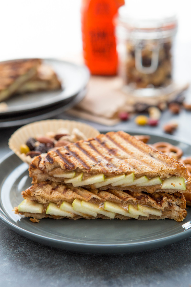 Grilled apple and peanut butter panini sandwiches on plates with Nate's honey bottle and nuts in the backdrop.