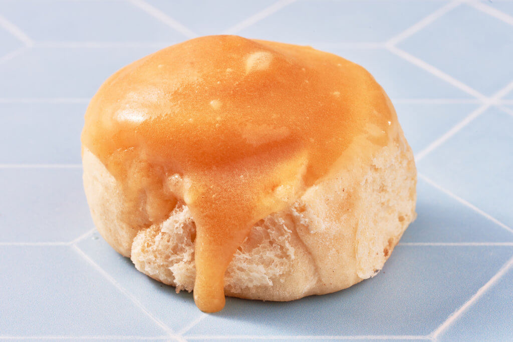 A bread roll topped with dripping honey  on a blue tiled countertop.