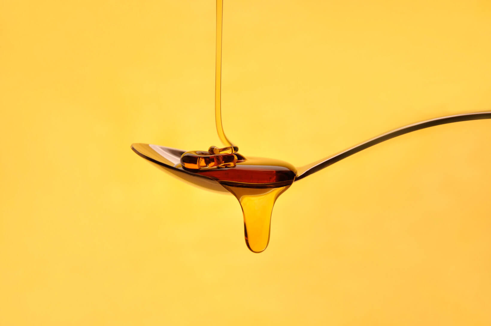 Dripping honey on spoon against yellow background.
