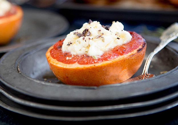Broiled grapefruit with melted ricotta cheese and a sprinkle of spices on dark plates.