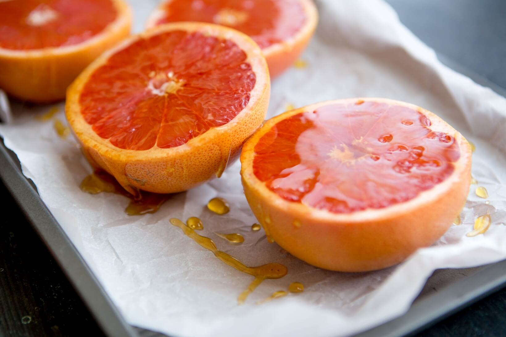 Halved grapefruits drizzled with honey on parchment paper.